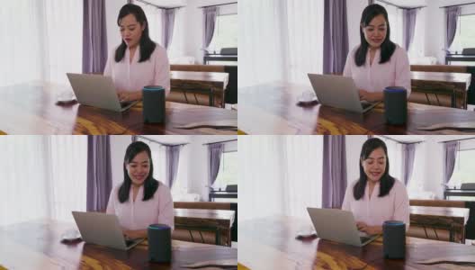 亚洲成熟女性在家里的客厅里使用笔记本电脑和智能扬声器工作高清在线视频素材下载