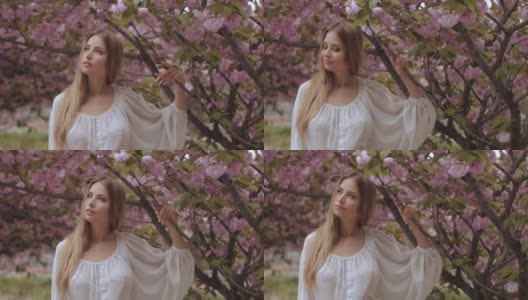 一个女人在自然盛开的樱花树的春天美丽肖像高清在线视频素材下载