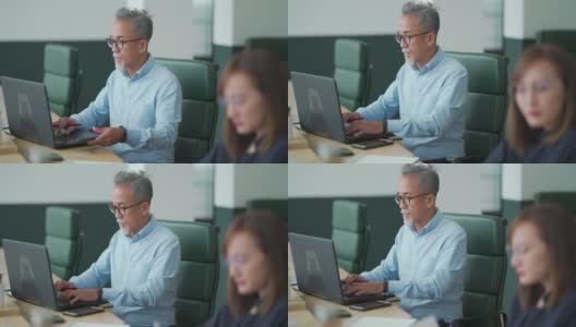 亚洲华人工作高级男子系使用笔记本电脑与他的同事在开放式办公室工作高清在线视频素材下载