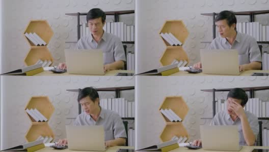 在家庭办公室工作的亚洲老人因业务压力过大。从笔记本电脑检查后高清在线视频素材下载