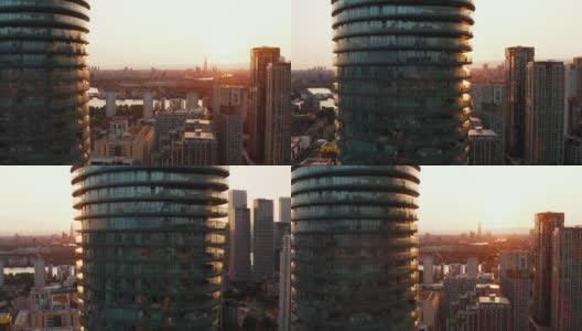 在金丝雀码头区高耸的现代圆柱形住宅建筑Arena Tower周围飞行。日落时分的未来城市区。英国伦敦高清在线视频素材下载
