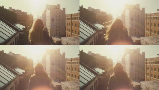 一个美丽的女人站在屋顶上，风吹散她长长的红头发。城市城市景观纽约市与伟大的摩天大楼和建筑物。高清在线视频素材下载