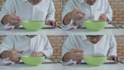 一名亚洲男子一边看书一边吃着绿色碗里的方便面。高清在线视频素材下载