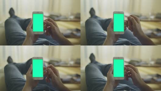 一名男子躺在家里的沙发上，用绿色屏幕竖屏打电话。高清在线视频素材下载