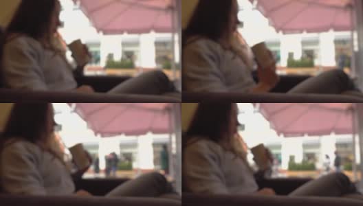 一个穿着迷彩服的黑发女孩在窗边的咖啡馆里用吸管喝着酒。全高清背景散景剪辑高清在线视频素材下载