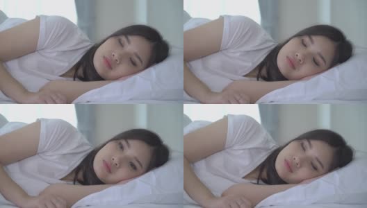 美丽的亚洲女人肖像与迷人的微笑享受新鲜柔软的床上用品亚麻布床垫在白色的卧室现代公寓。可爱的亚洲女孩睡觉休息，晚安睡眠的概念。高清在线视频素材下载