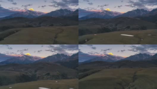 连绵不断的草原后面，雪山的山顶被日出的光芒所照亮高清在线视频素材下载