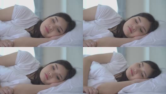 美丽的亚洲女人肖像与迷人的微笑享受新鲜柔软的床上用品亚麻布床垫在白色的卧室现代公寓。可爱的亚洲女孩睡觉休息，晚安睡眠的概念。高清在线视频素材下载