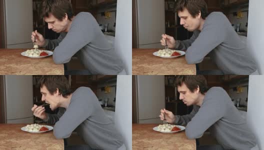 男人用叉子吃饺子，把它们放进厨房的番茄酱里。高清在线视频素材下载