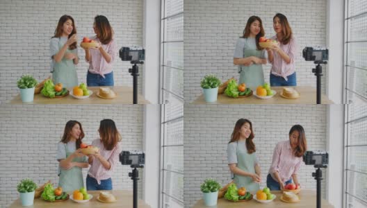 两个年轻的亚洲女性美食博主拿着红苹果，解释健康的饮食和健康的生活方式，同时录制视频供广播，Vlog健康的生活方式高清在线视频素材下载
