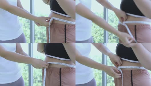 年轻女性教练在健身时与腰围大的女性测量大体型层高清在线视频素材下载
