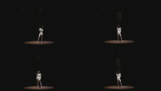 一个美丽的歌手在黑暗的舞台上在白色聚光灯下。高清在线视频素材下载
