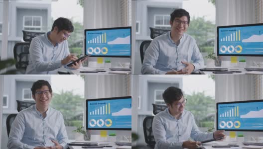 肖像头的年轻有吸引力的亚洲男子坐在微笑工作的多屏幕电脑和智能平板电脑在桌子上在家里的概念自由职业者数据分析师，数据科学家的业务。高清在线视频素材下载