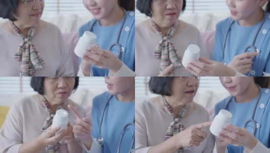 在家访护理服务中，年轻的护理人员穿着手术服向年长的亚洲妇女展示药瓶。亚洲老年人与辅助生活药物监测坐在家里交谈。高清在线视频素材下载