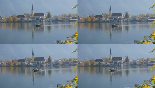 在德国巴伐利亚州泰根西湖风景如画的美丽教堂背景下，一名船夫将人们摆渡到另一边高清在线视频素材下载