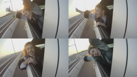 快乐迷人的女人在夕阳西下时，在汽车的后座上愉快地挥手，她的头伸出窗外高清在线视频素材下载