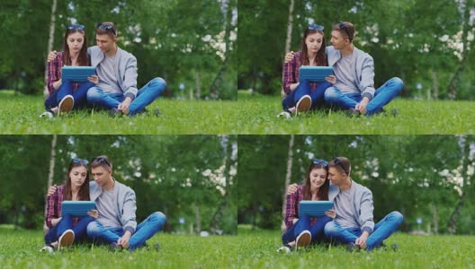年轻女孩和一个男孩在公园里用平板电脑，男孩拥抱女孩高清在线视频素材下载