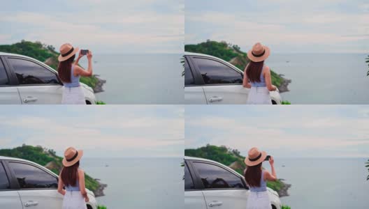 年轻的女性旅行者看着和拍照在美丽的海景与她的车，而旅行驾驶公路旅行的假期高清在线视频素材下载