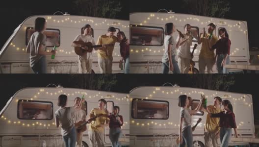 一群亚洲男女朋友在晚上的户外聚会上一起弹吉他。朋友们带着幸福和微笑碰杯喝啤酒。乘露营车旅行大自然。高清在线视频素材下载