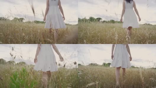 电影慢镜头与底部视角的POV场景，无法辨认的年轻女子与波西米亚白裙子走在高高的草地鲜花在日落看着地平线。春天和夏天高清在线视频素材下载