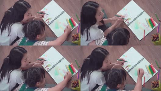 妈妈正在帮她的女儿做家庭作业和在书上涂色。艺术教育和创意活动地板。高清在线视频素材下载
