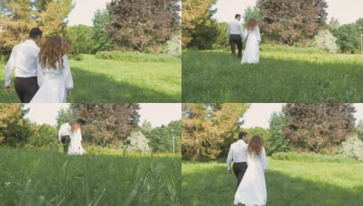 一位年轻女子和一位身穿白色西装的男子在公园里散步。牵手，在模糊地带。高清在线视频素材下载