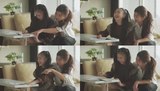 亚洲华人年轻的家庭母亲和女儿周末在客厅公寓里做家庭作业，享受亲子时光高清在线视频素材下载