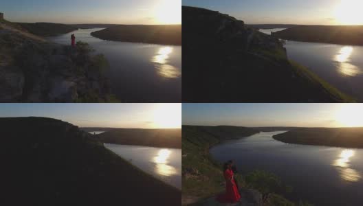 从空中飞离的情侣站在悬崖边靠近水边。穿着红色裙子的女人。人黑。日落高清在线视频素材下载