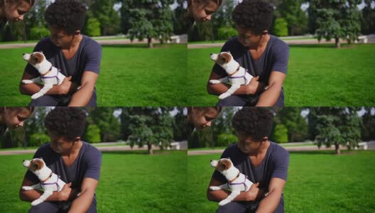 两个多种族的年轻朋友坐在公园的草地上享受这一天，同时抱着可爱的小杰克罗素梗和微笑。快乐的夏天高清在线视频素材下载