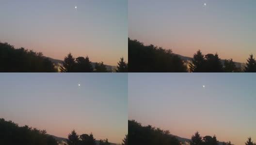 月亮在晴朗的蓝色夜空下，后面是一些剪影的树高清在线视频素材下载