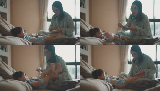 快乐的妈妈和可爱的男孩在卧室里玩医生游戏。高清在线视频素材下载