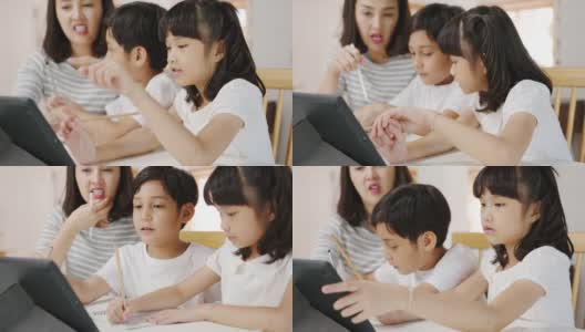 快乐亚洲家庭家庭教育，母亲教孩子在家里的客厅使用数码平板电脑。高清在线视频素材下载