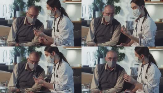 年轻漂亮的女医生向65-70岁戴着医用口罩的快乐老人展示装有疫苗的烧瓶高清在线视频素材下载