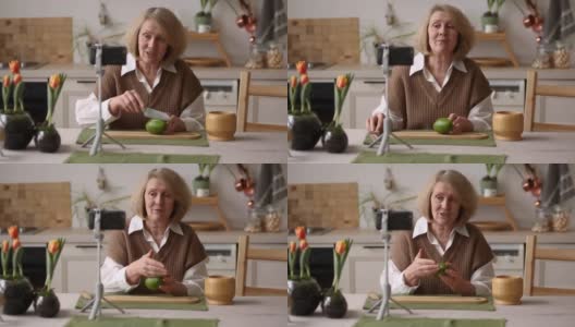 一位年长的女性美食博主一边在手机上展示食材，解释鳄梨的食谱，一边录制视频或在家里的厨房里为博客播放高清在线视频素材下载
