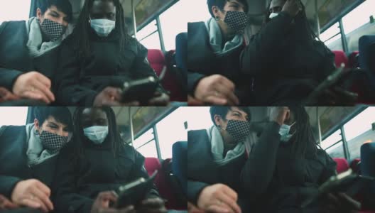 一名戴面具的黑人男子和一名戴面具的白人女子在公交车上看手机屏幕。高清在线视频素材下载