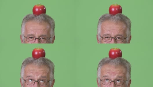 在绿色背景下，一名年长男子头顶苹果的大头照高清在线视频素材下载