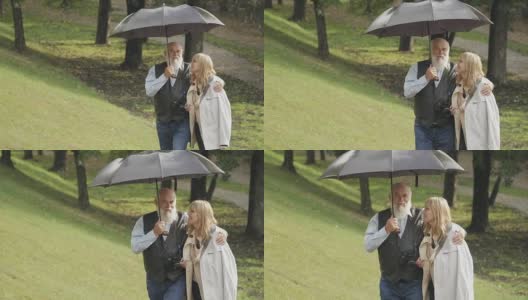 一位快乐的年轻女子和一位老人在雨中雨伞下在公园散步高清在线视频素材下载
