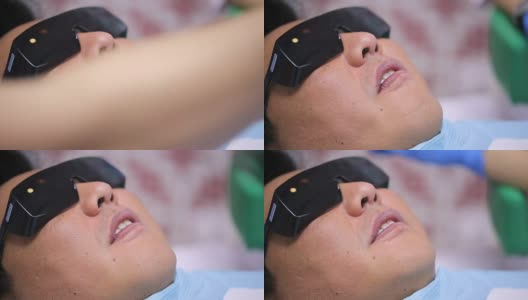 在紫外线辐射下戴墨镜的亚洲人男性病人在牙科椅上张开他的嘴高清在线视频素材下载