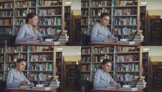 美丽严肃的白人女学生坐在桌子上的书在图书馆用笔记本电脑在抄写总结高清在线视频素材下载