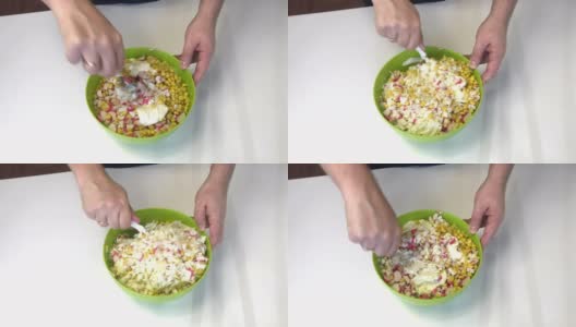 一个男人在做沙拉。将剁碎的蟹棒，玉米，北京卷心菜和蛋黄酱混合在一个容器里。高清在线视频素材下载