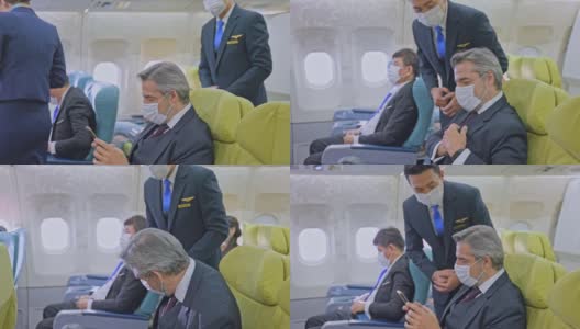新冠肺炎疫情期间戴口罩乘坐飞机预防感染的白种商务旅客。乘务员通知乘客关闭电子设备。高清在线视频素材下载