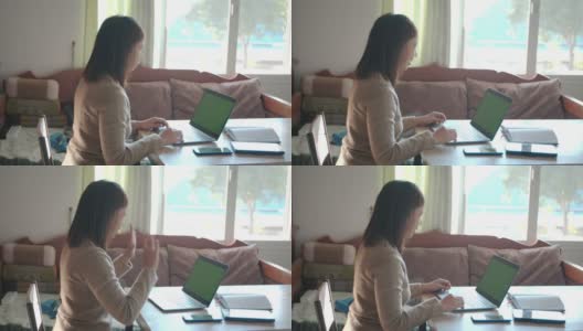 一名年轻的亚洲女子在家里的绿屏笔记本电脑上向参加网络会议的同事问好。在家工作的女性员工。高清在线视频素材下载