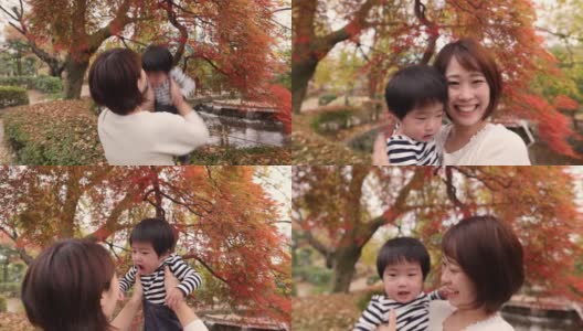 年轻的母亲在秋天的红叶下捡起她的宝贝儿子高清在线视频素材下载