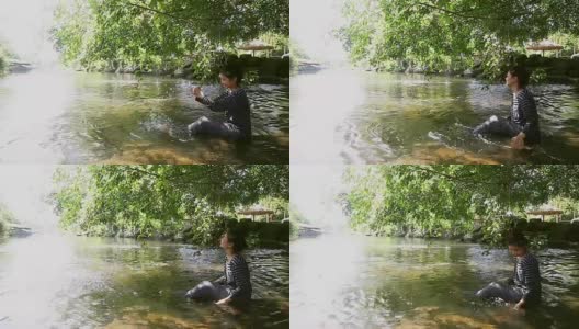 小女孩坐在小溪边，独自捡起水玩高清在线视频素材下载