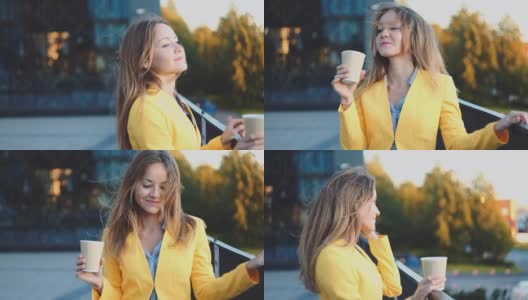年轻漂亮的女孩穿着黄色夹克在办公室附近停留，微笑着在阳台上喝着咖啡。商务中心微笑着喝茶的商务女性。早晨明亮的阳光高清在线视频素材下载