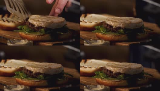 男性的手把camembert奶酪与酱汁和绿色植物自制汉堡包，食物色情的概念。资料片。准备肥美的汉堡高清在线视频素材下载