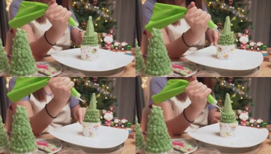 亚洲妇女的手从奶油榨汁机榨取绿色奶油，在自制的圣诞树上做成树叶，作为庆祝圣诞节的甜点，12月假日在公寓里装饰圣诞树，礼盒，圣诞老人。高清在线视频素材下载