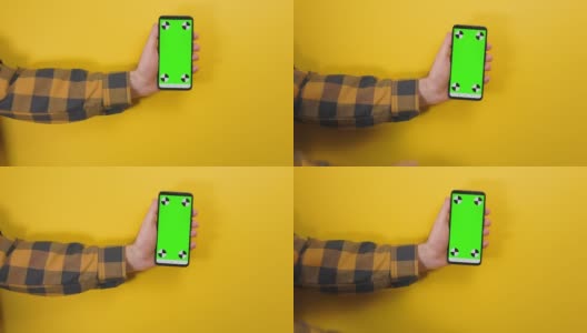 男人的手拿着一个带有垂直绿色色度键屏幕的手机，另一只手在触屏上滑动。黄色背景。智能手机应用的概念高清在线视频素材下载