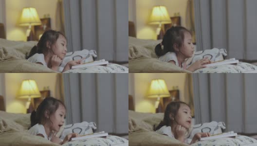 可爱的5岁亚洲女孩正在看书，躺在床上，有一盏灯发出美丽的黄色灯光。它是儿童学习、放松和发展创造力的睡前故事。高清在线视频素材下载
