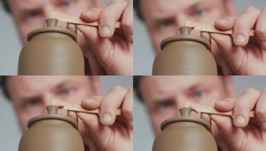 一个男性陶工的特写镜头，从一个陶工的车轮上的一个陶土茶壶的壶盖的把手中去除多余的粘土。陶工制作粘土制品高清在线视频素材下载